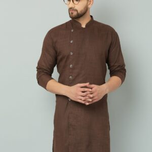 Man in Indian brown kurta and white pants sitting on stool.