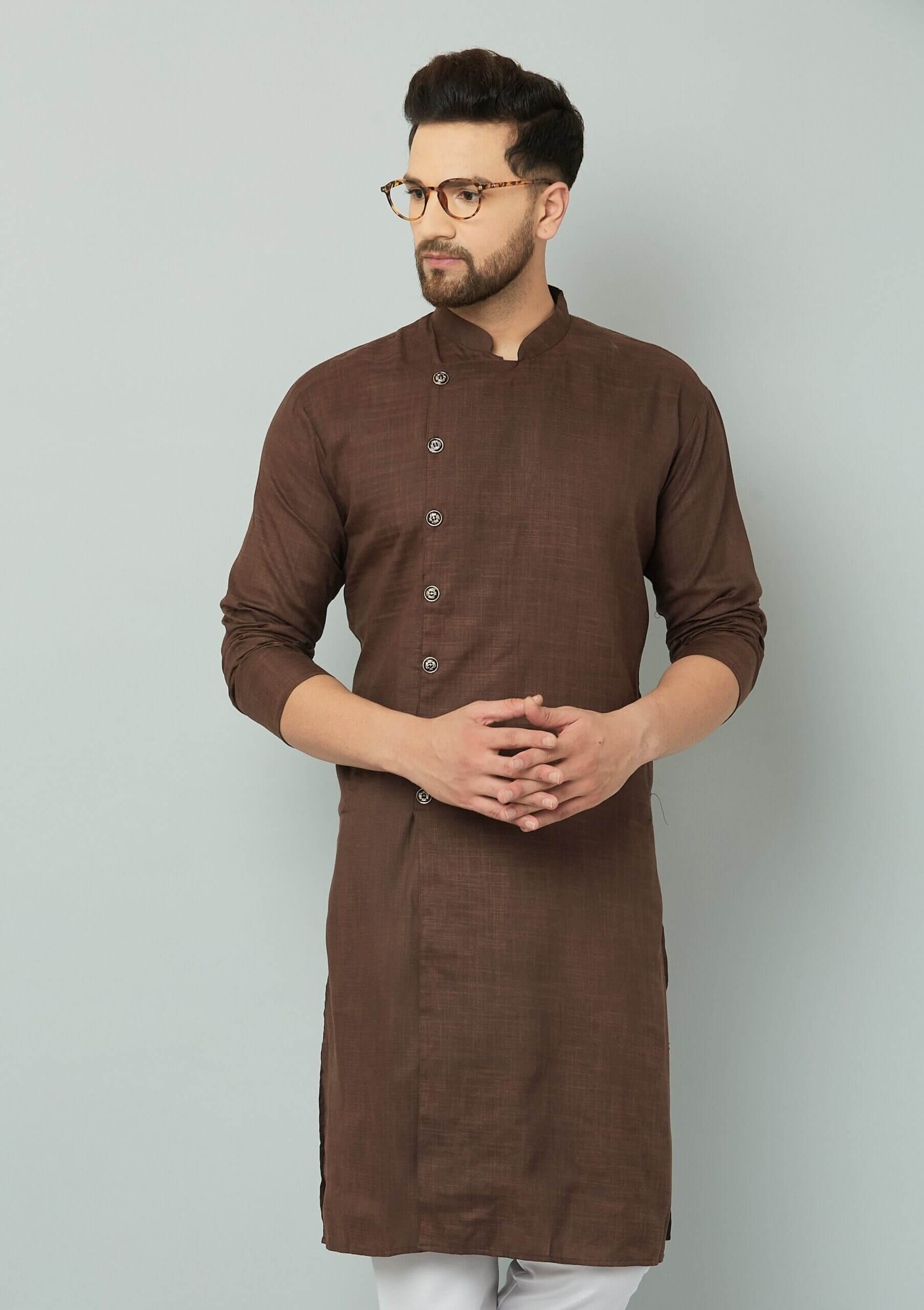Stylish Assymetric Sherwani Style Kurta Man in Indian brown kurta and white pants sitting on stool.